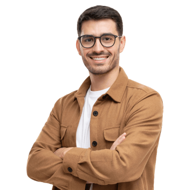 Moški z očali veselo stoji z prekrižanimi rokami, oblečen je v belo majico in rjavo jakno