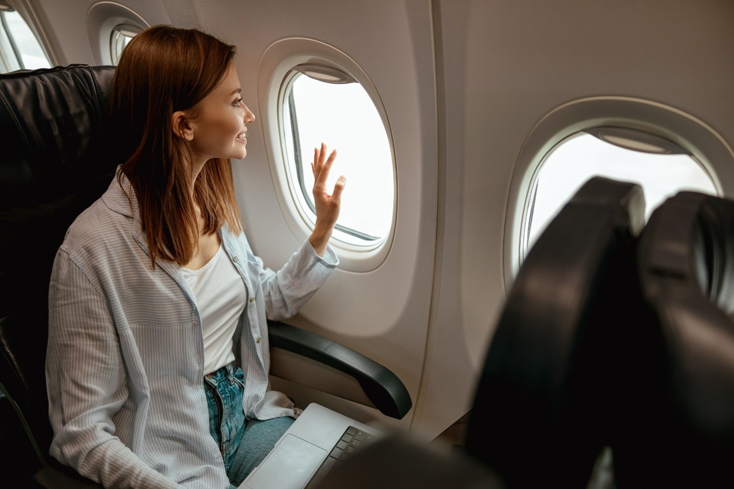 Ženska, oblečena v belo bluzo, vesela in umirjena sedi v letalu in gleda skozi okno